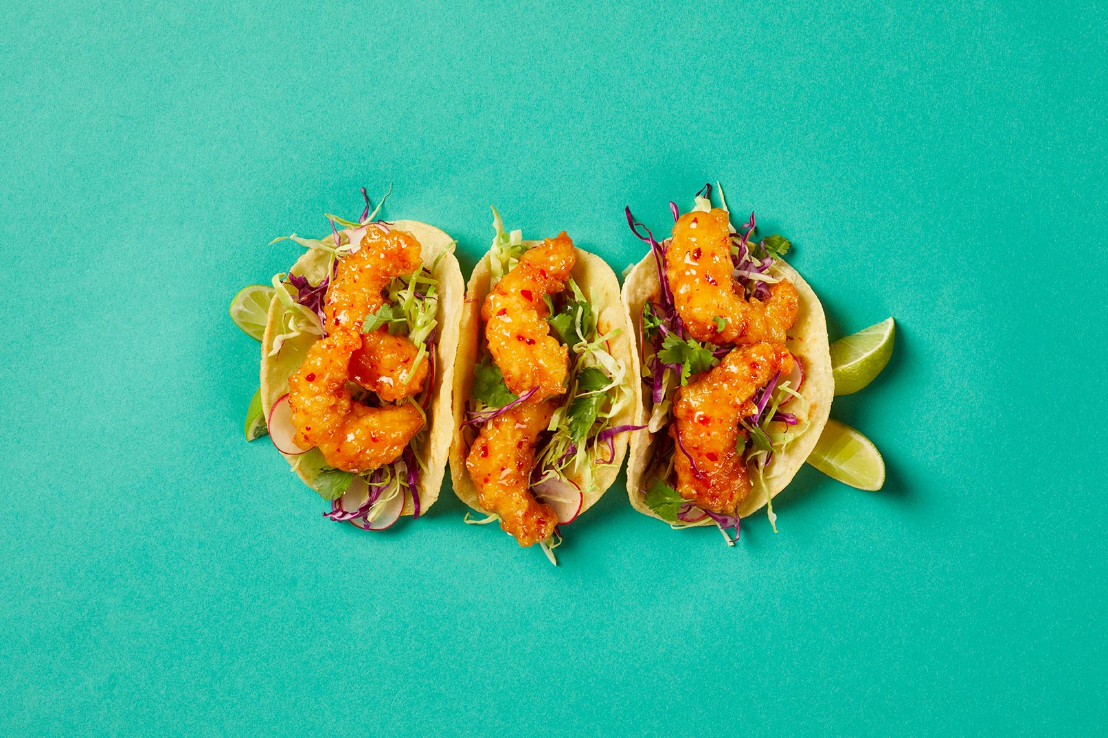 Three Crispy Shrimp Tacos with limes on the side