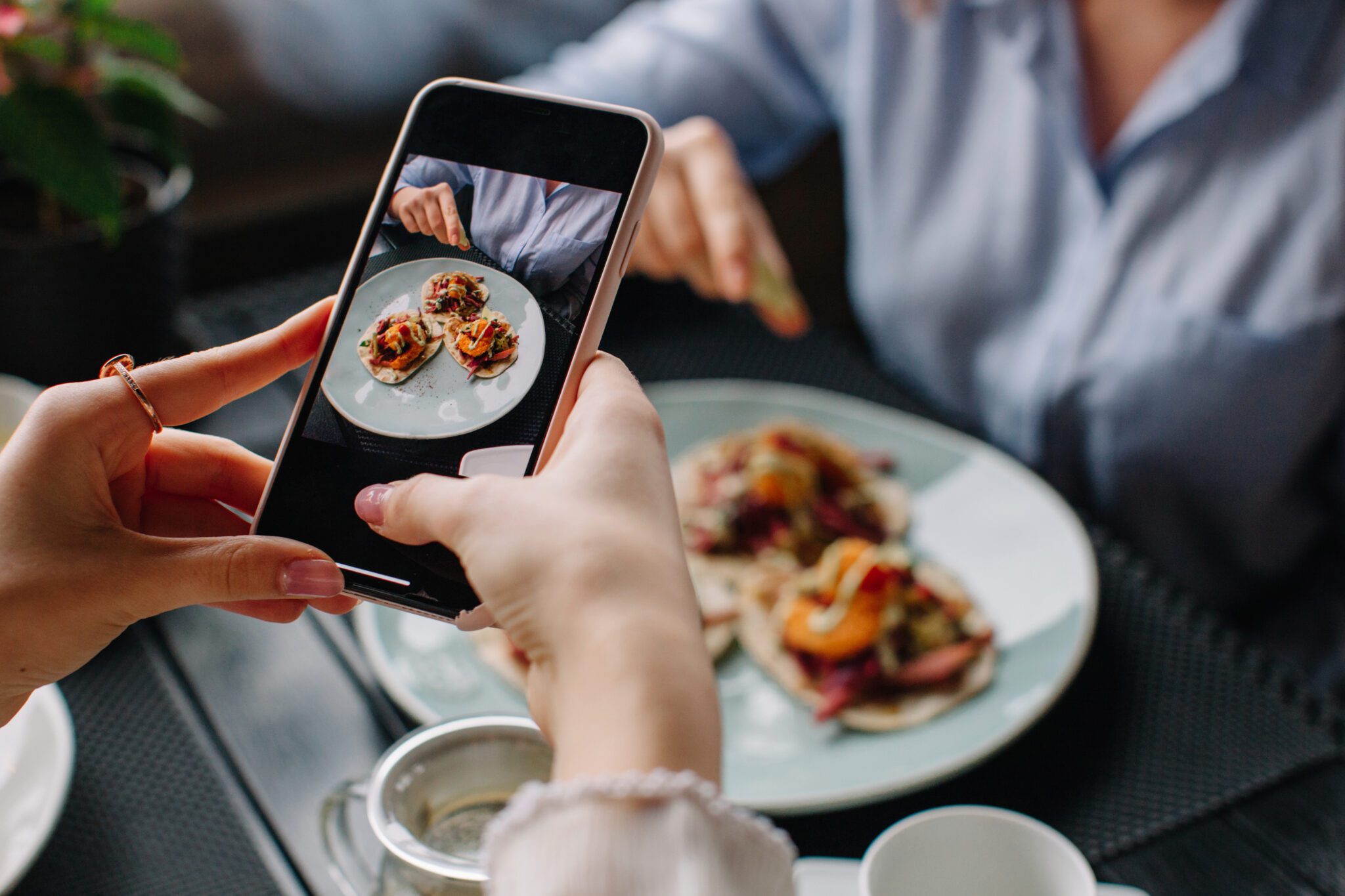 Woman taking picture of tasty tacos with her phone at cafe