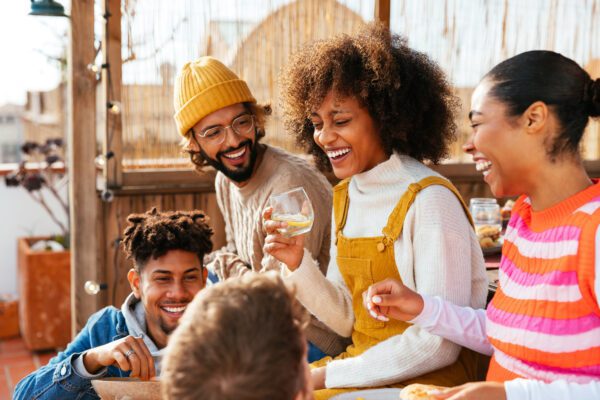 Positive young men and women in casual clothes sitting on bench and looking at each other while laughing at joke in a rooftop