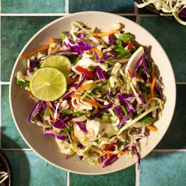 Overhead view of asian-inspired slaw recipe in a white bowl over a green tile surface.