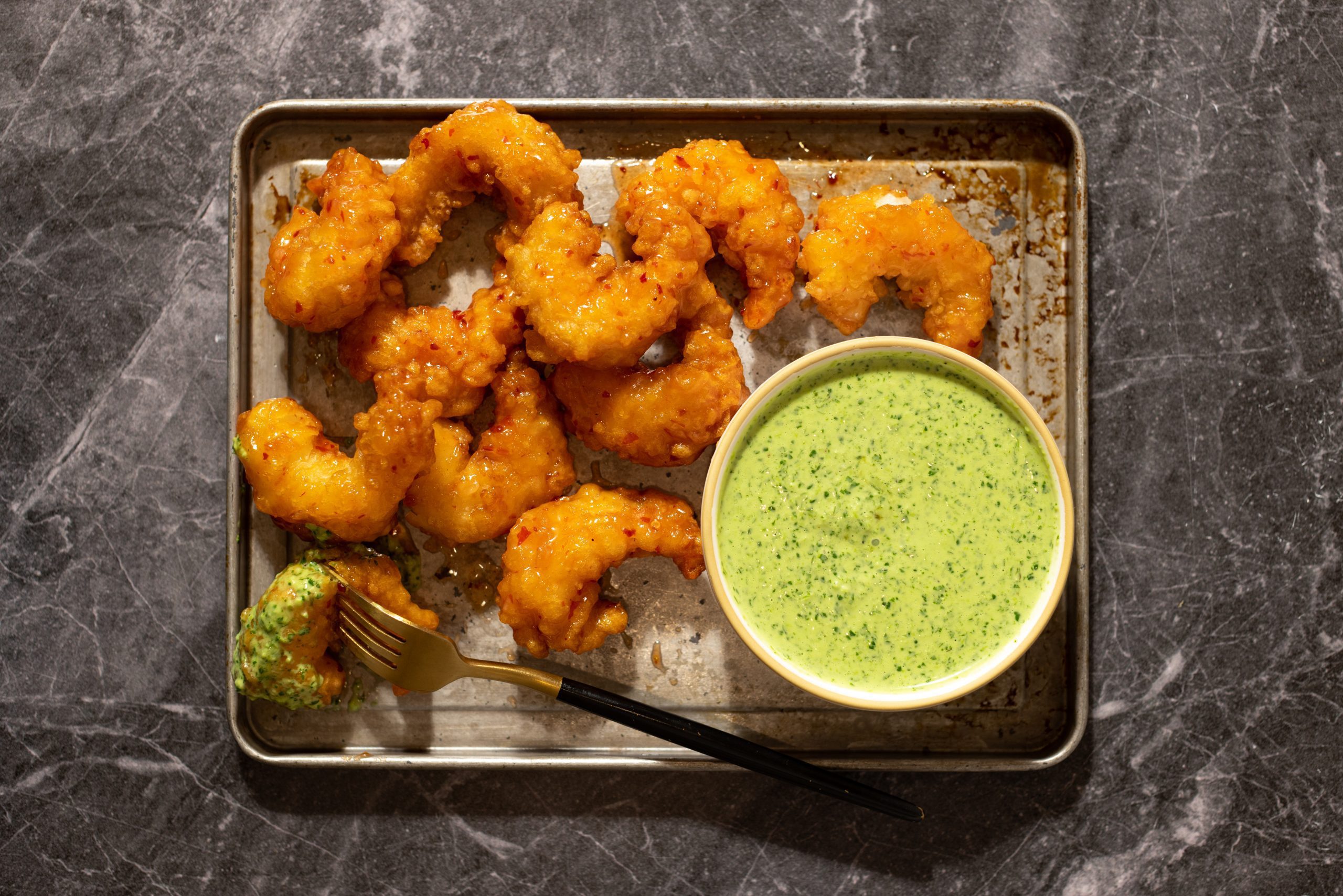 Bowl of Peruvian Aji Verde Sauce served with Sweet & Spicy shrimp on metal baking tray over a granite surface tabletop.