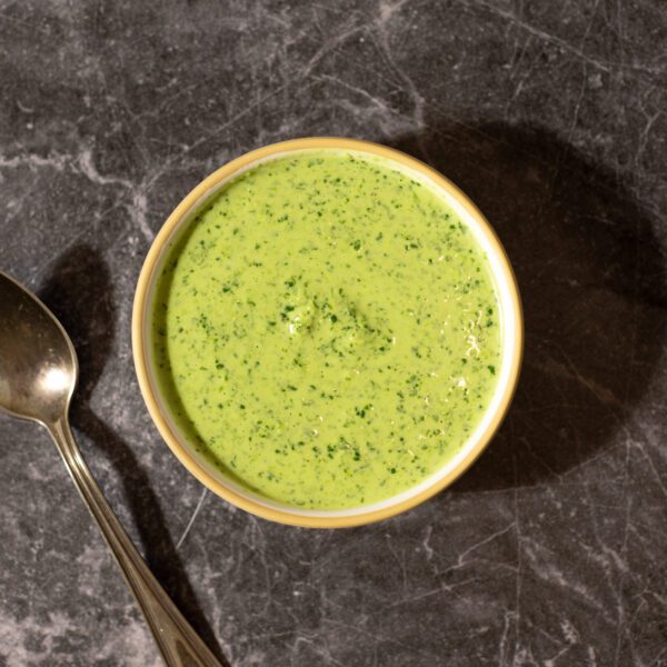 Peruvian Aji Verde Sauce served in a white bowl with a spoon resting on a dark granite surface tabletop.