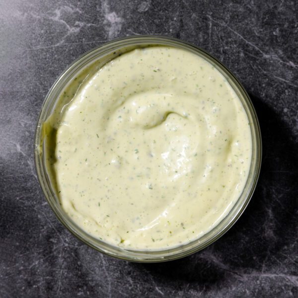 Overhead view of a herby aioli dip served in a clear bowl over a dark gray marble surface.