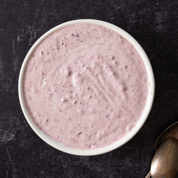 Overhead view of a white bowl filled with Kalamata Olive Aioli, served over a dark granite surface.