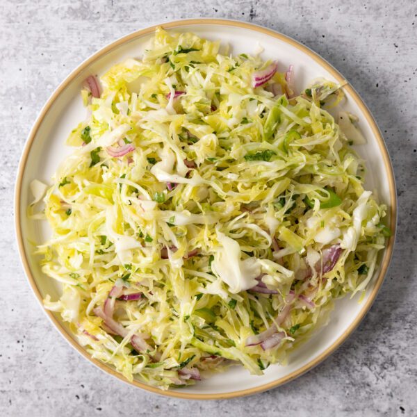 Overhead view of white plate filled with spicy serrano slaw, served over a white gray textured surface.