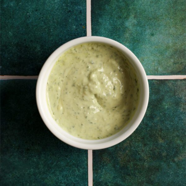 Overhead view of a white bowl filled with pesto aioli, served over a green tiled surface.