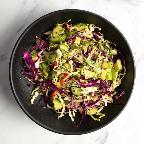 Overhead view of an Asian-inspired chopped salad on a black plate served over a marble tabletop.