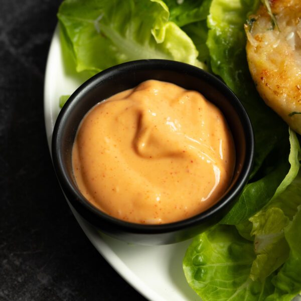 Ginger Gochujang Aioli in a small round black sauce dish atop a plate of lettuce.