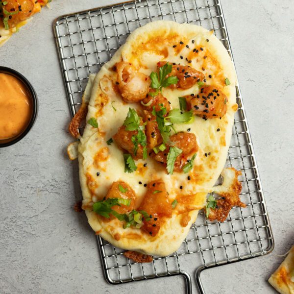 Sweet and spicy shrimp flatbread pizza on a metal handled rack with aioli sauce cropped off the side.