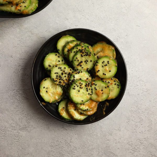 Overhead view of a black bowl of peanut cucumber salad, served over a white gray stone surface.