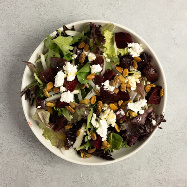 Overhead view of a beet & goat cheese salad on a white plate over a white textured tabletop.