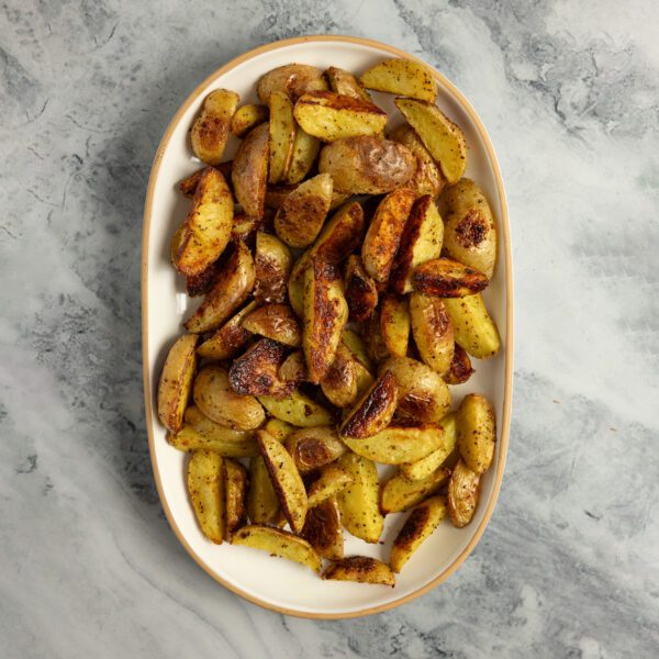 Overhead view of a large platter of crispy adobo potato wedges served over a marble tabletop.