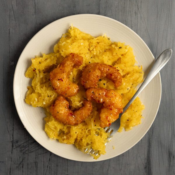 Overhead view of garlic butter spaghetti squash with sweet & spicy shrimp on a white plate with a fork, served over a gray textured tabletop.