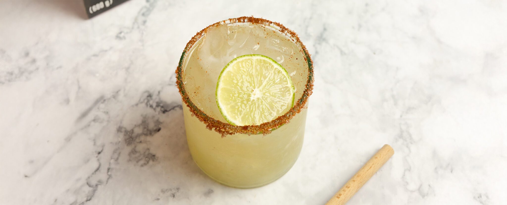 Three quarter angle view of Sweet & Spicy Margarita in a clear glass with a chili salted rim and lime slice garnish.