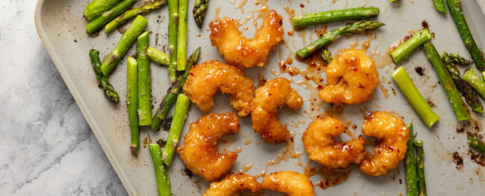 Overhead view of a sheet pan of roasted asparagus and Social Kitchens Sweet & Spicy shrimp.
