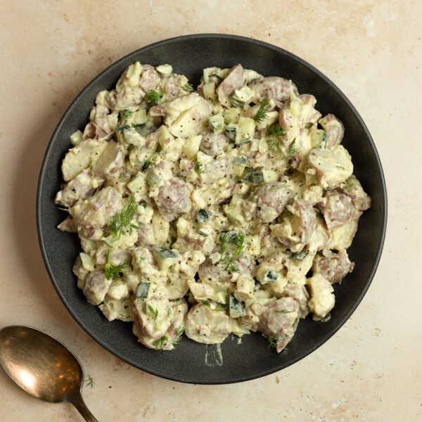 Overhead view of a black plate full of Mediterranean Potato Salad garnished with dill and a brass spoon off to the side. Served over a beige marble tabletop.