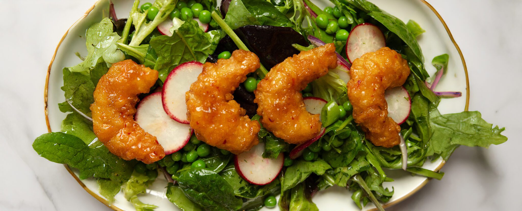 Overhead view of a Spring Pea Salad with four pieces of Social Kitchens Sweet & Spicy Shrimp on top.