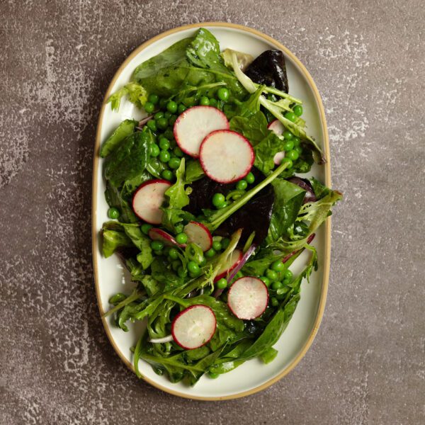 Overhead view of a Spring Pea Salad on a large white ceramic platter over a gray stone tabletop.