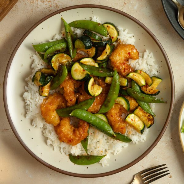 Overhead view of summer veggies & shrimp sheet pan meal over rice on a white plate.