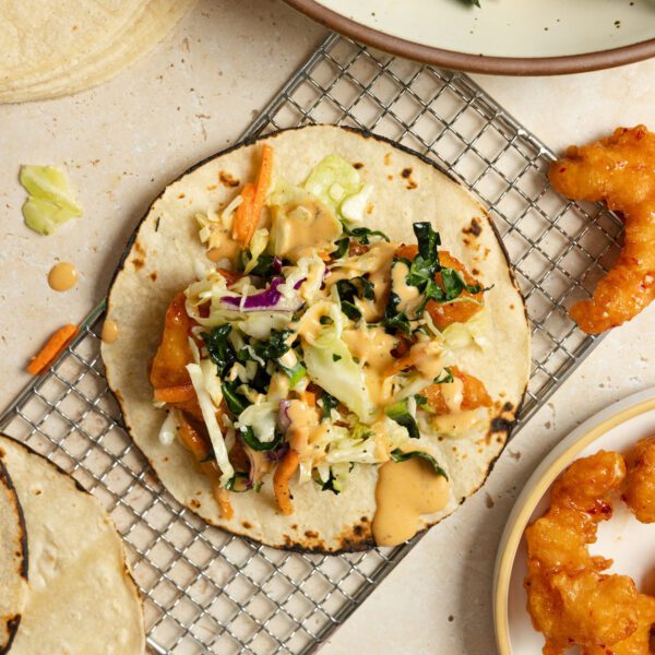 Overhead view of Social Kitchens Sweet & Spicy Shrimp tacos with slaw, served on a wire rack with ingredients scattered around the tabletop.
