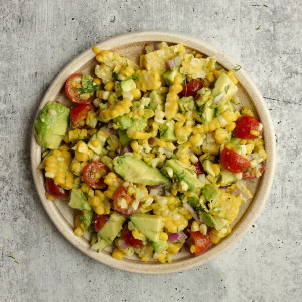 Overhead view of a white ceramic plate of Corn & Avocado Salsa, served over a textured light gray stone tabletop.