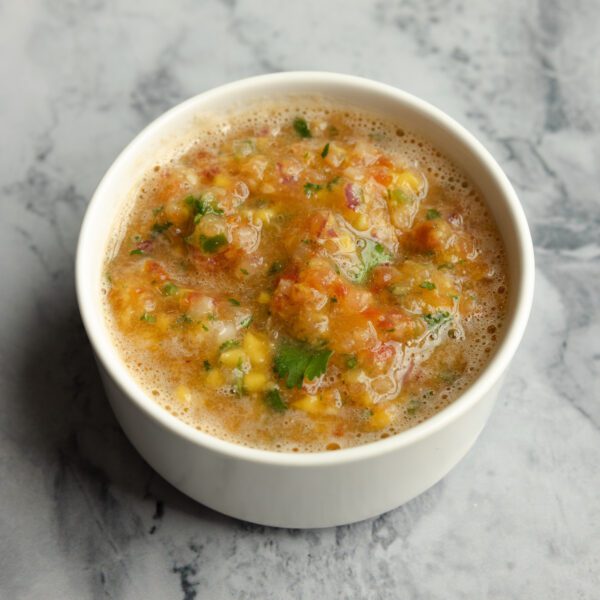 Three-quarter view of a white ramekin bowl of mango salsa, served over a marble tabletop.
