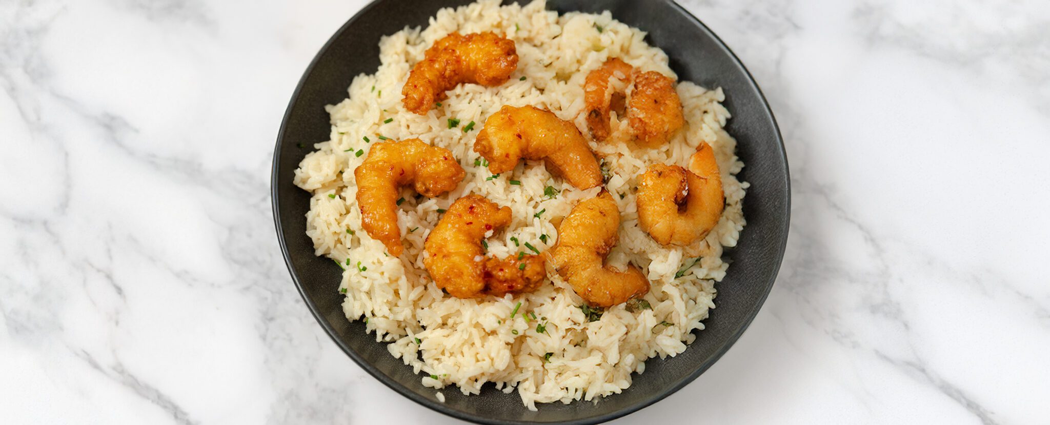 Overhead view of Chive Bone Broth Rice with Social Kitchens Sweet & Spicy Shrimp in a black bowl over a marble tabletop.