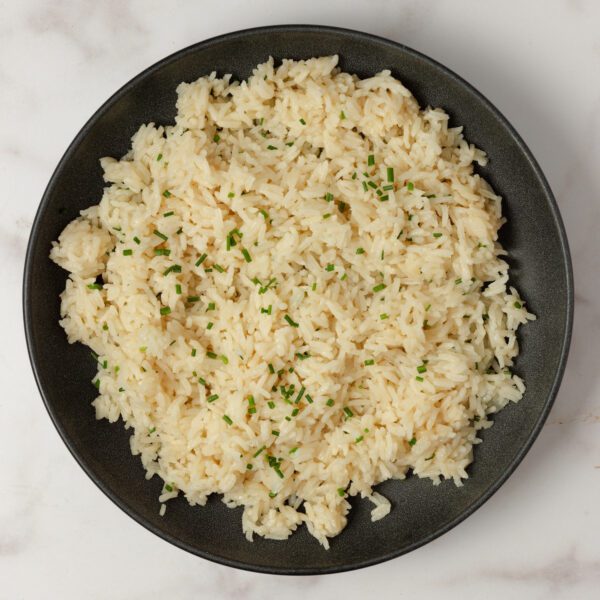 Overhead view of Chive Bone Broth Rice in a black bowl over a marble tabletop.