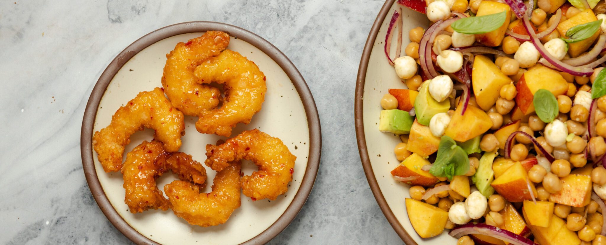 Overhead view of two plates. The smaller plate has Social Kitchens sweet & spicy shrimp. The larger plate has a summer peach salad.