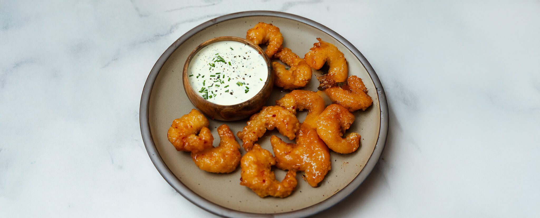 A round plate with Social Kitchens Sweet & Spicy Shrimp with a side of chive aioli, served on a marble tabletop.
