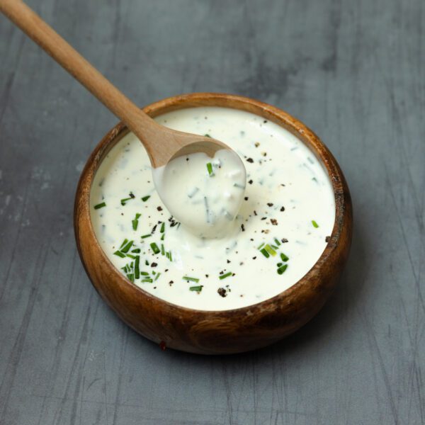 A wooden bowl filled with Chive Aioli with a wooden spoon on a gray tabletop.