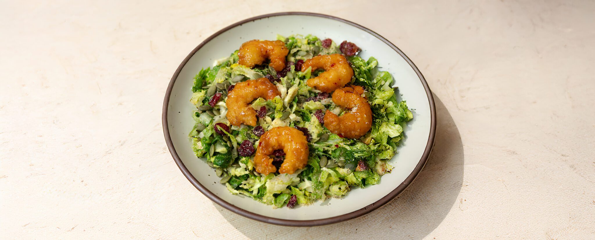 Three-quarter view of a fall caesar salad with Social Kitchens Sweet & Spicy Shrimp placed on top.