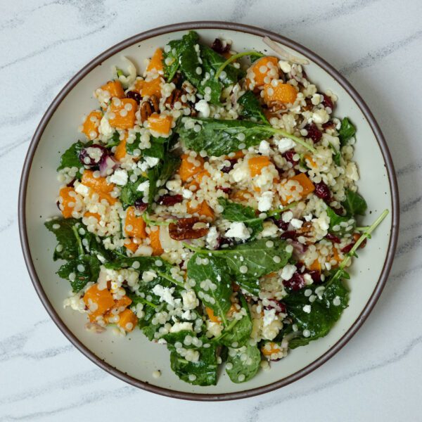 Overhead view of a white plate of fall couscous salad topped with Social Kitchens Sweet & Spicy Shrimp, served on a marble tabletop.
