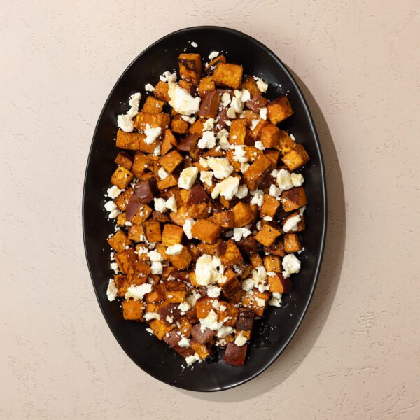 Overhead view of roasted chipotle sweet potatoes with feta on a large black platter.