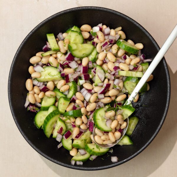 Overhead view of Lemon Dill Bean Salad in a black bowl with a spoon sticking out.