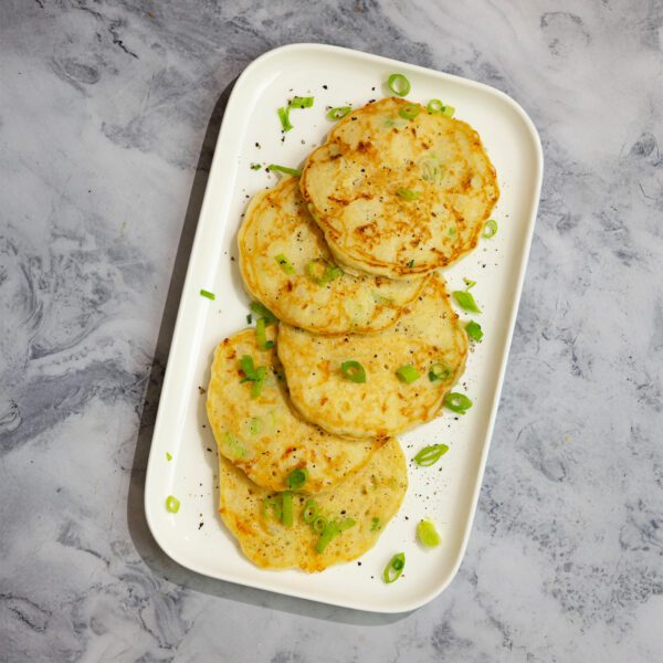 Overhead view of savory scallion pancakes on a rectangular plate, garnished with scallions and served on a marble tabletop.