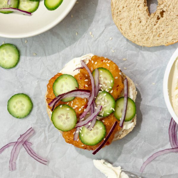 Overhead view of Social Kitchens Sweet & Spicy Shrimp Bagels, garnished with cucumbers and red onion.