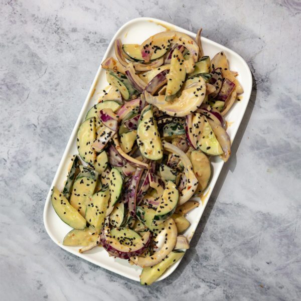 Overhead view of a large white rectangular plate of Tahini Cucumber Salad, served on a marble tabletop.