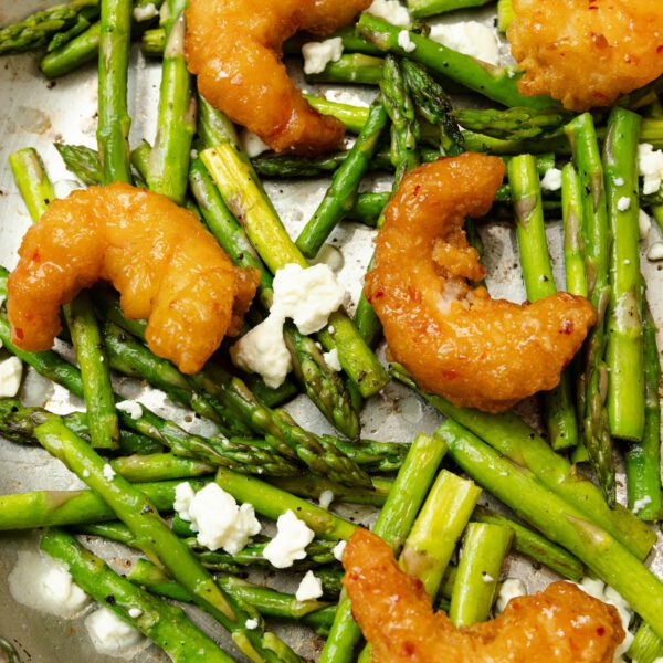 Overhead close-up view into a stainless steel pan of lemon feta asparagus with Social Kitchens Sweet & Spicy Shrimp.