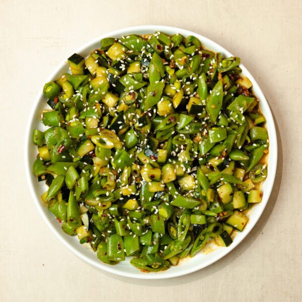 Overhead view of snap pea salad garnished with sesame seeds on a round white plate over a cream tabletop.
