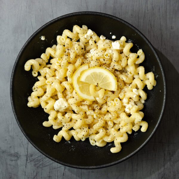 Overhead view of Lemon Feta Pasta in a round black bowl and garnished with a couple slices of lemon.
