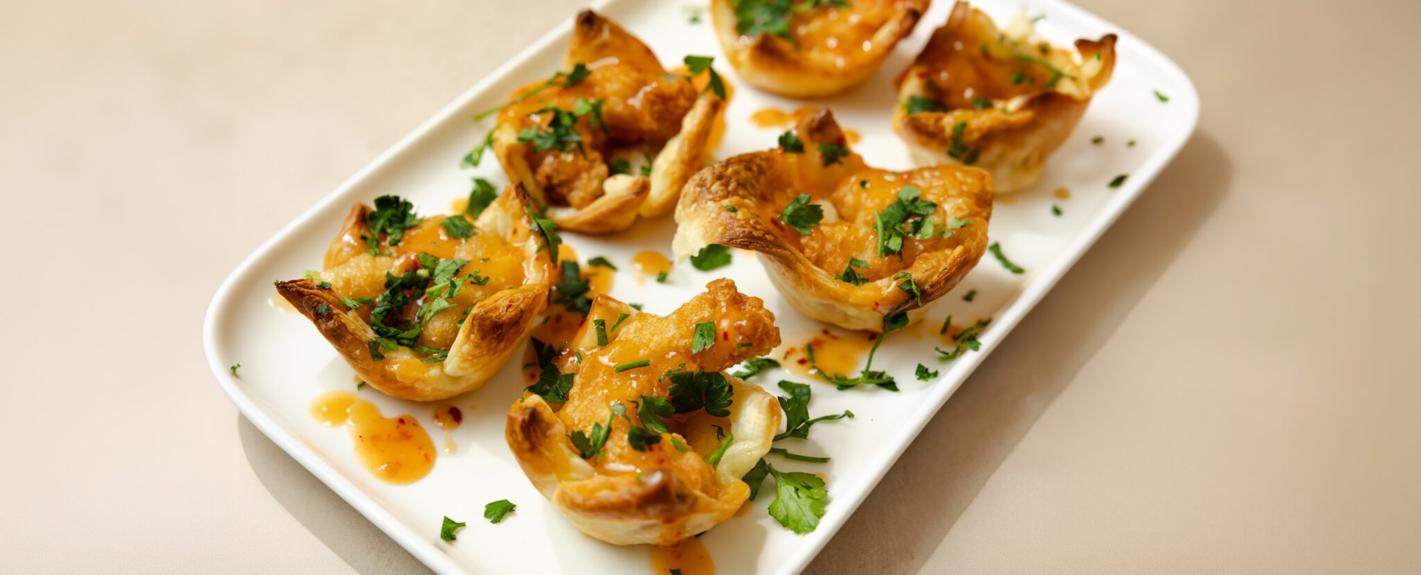 Three-quarter view of six Sweet & Spicy Puff Pastry Shrimp Cups served on a white rectangular dish.