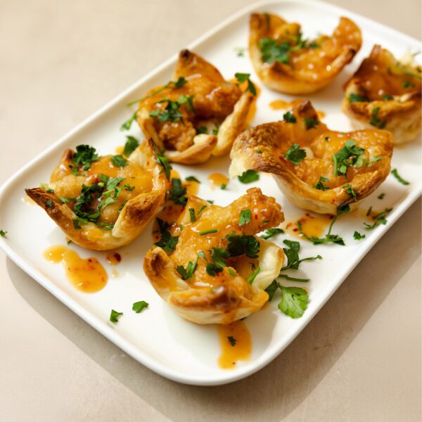 Three-quarter view of six Sweet & Spicy Puff Pastry Shrimp Cups served on a white rectangular dish.