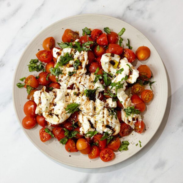 Overhead view of a white plate containing Burrata Caprese, served over a marble tabletop.