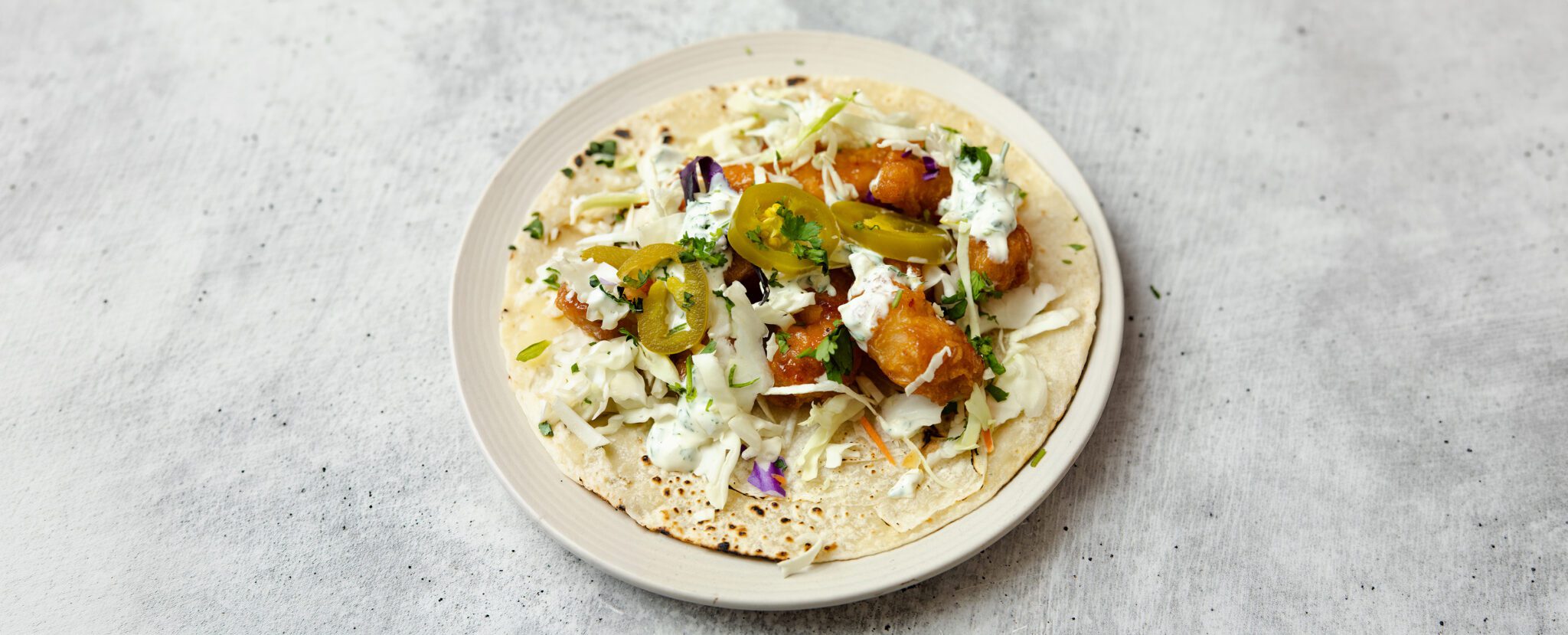 Three-quarter angle view of a Sweet & Spicy Shrimp Soft Taco on a round cream plate over a stone tabletop.