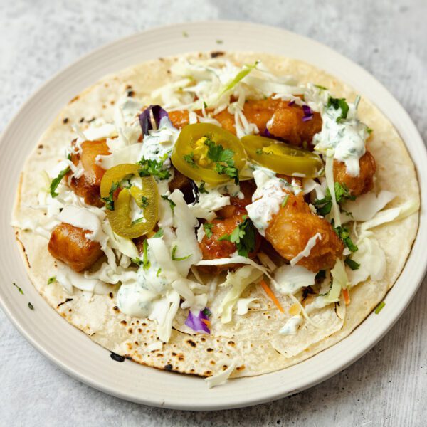 Three-quarter angle view of a Sweet & Spicy Shrimp Soft Taco on a round cream plate over a stone tabletop.