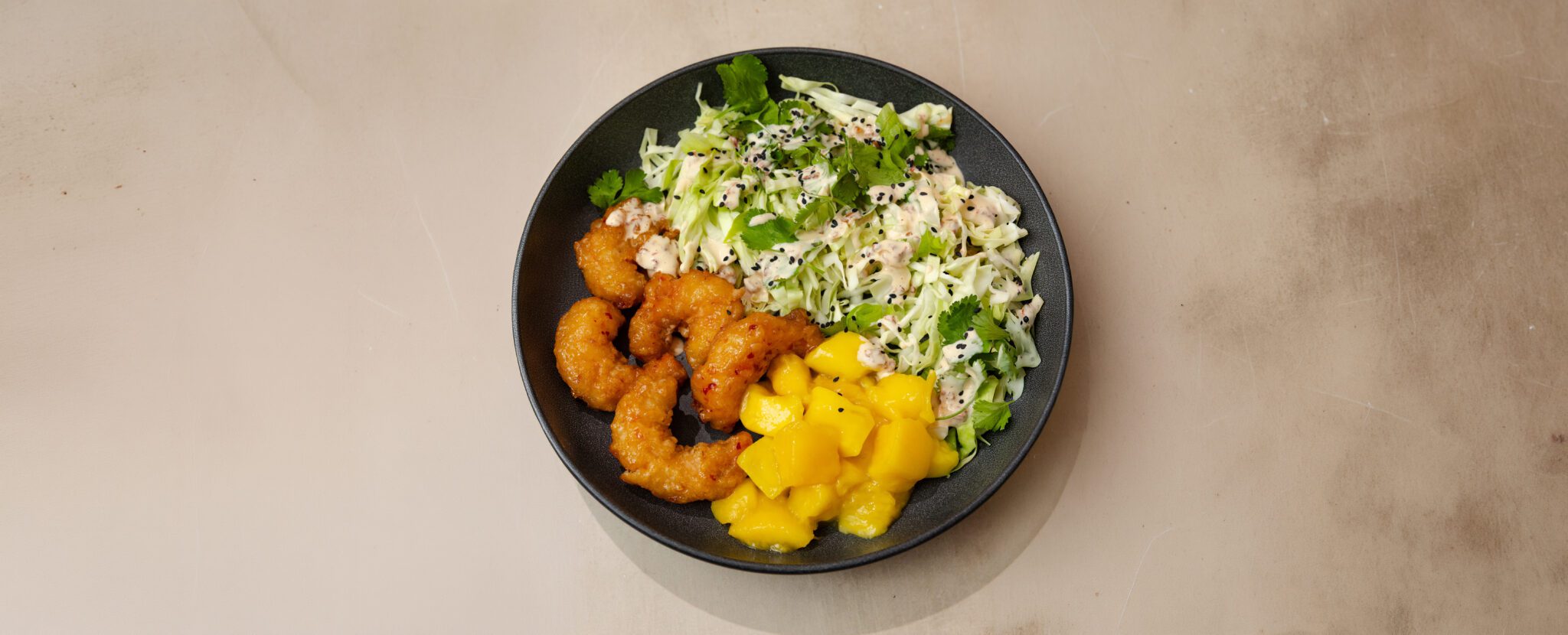 Three-quarter angle view of a Crunchy Mango Shrimp Bowl with crisp cabbage, juicy mango, and crunchy shrimp.