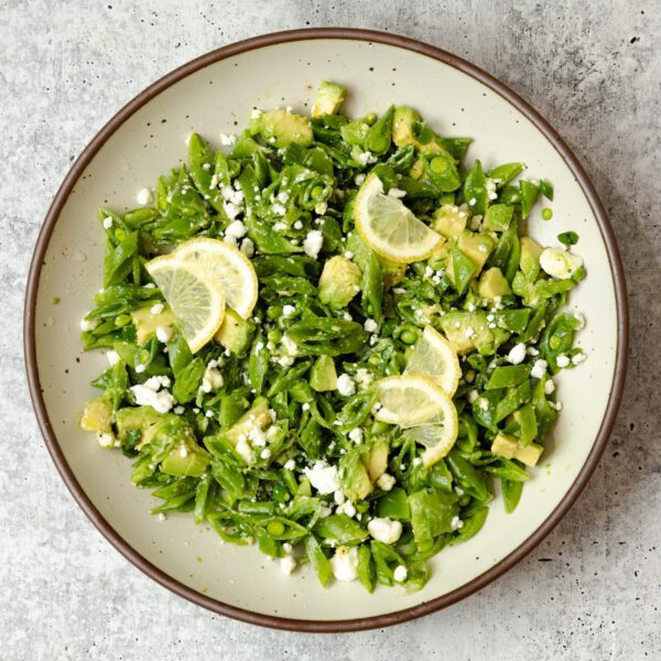 Overhead view of a Snap Pea & Avocado Salad on a round plate, served over a textured stone tabletop.