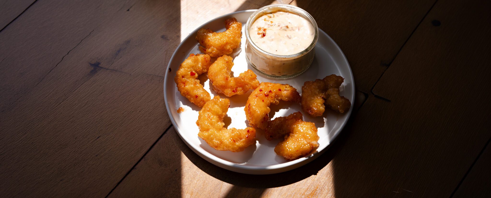 Three-quarter angle view of a plate of Social Kitchens Sweet & Spicy shrimp with a side of Spicy Chipotle Aioli.