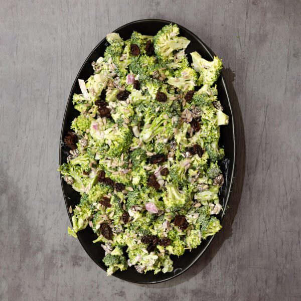 Overhead view of a large oval plate with Sweet & Crunchy Broccoli Salad, served over a gray wood tabletop.